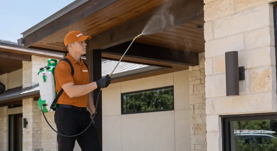 Bastion Pest Control technician treating eaves and soffits with a backpack sprayer so wasps cannot rebuild