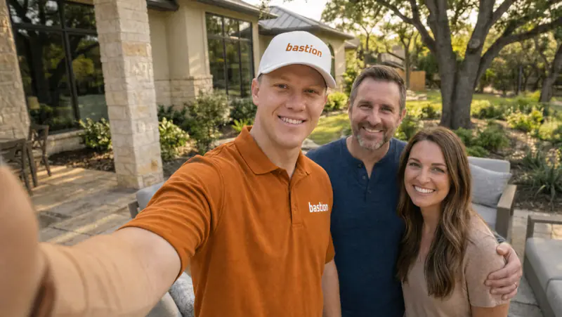 Bastion Pest Control technician in an orange polo and white cap taking a selfie with two homeowners on the patio outside their Austin, TX home