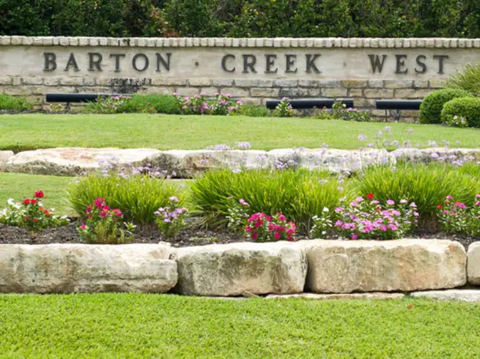 Barton Creek West stone entrance wall above limestone boulder beds and flowers, West Lake Hills area, Texas