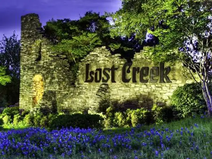 Lost Creek stone tower entrance sign above a field of bluebonnets, West Lake Hills area, Texas