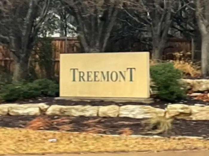 Treemont neighborhood sign set in limestone boulders in front of bare winter trees, West Lake Hills area, Texas