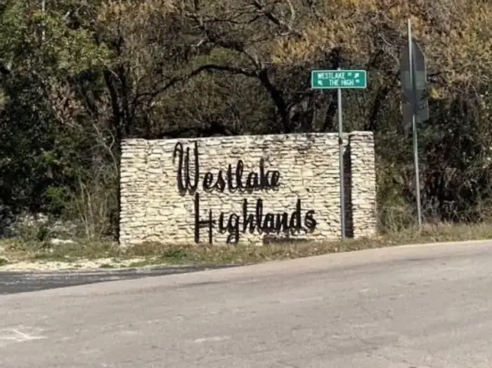 Westlake Highlands script sign on a stacked limestone wall at a wooded corner in West Lake Hills, Texas